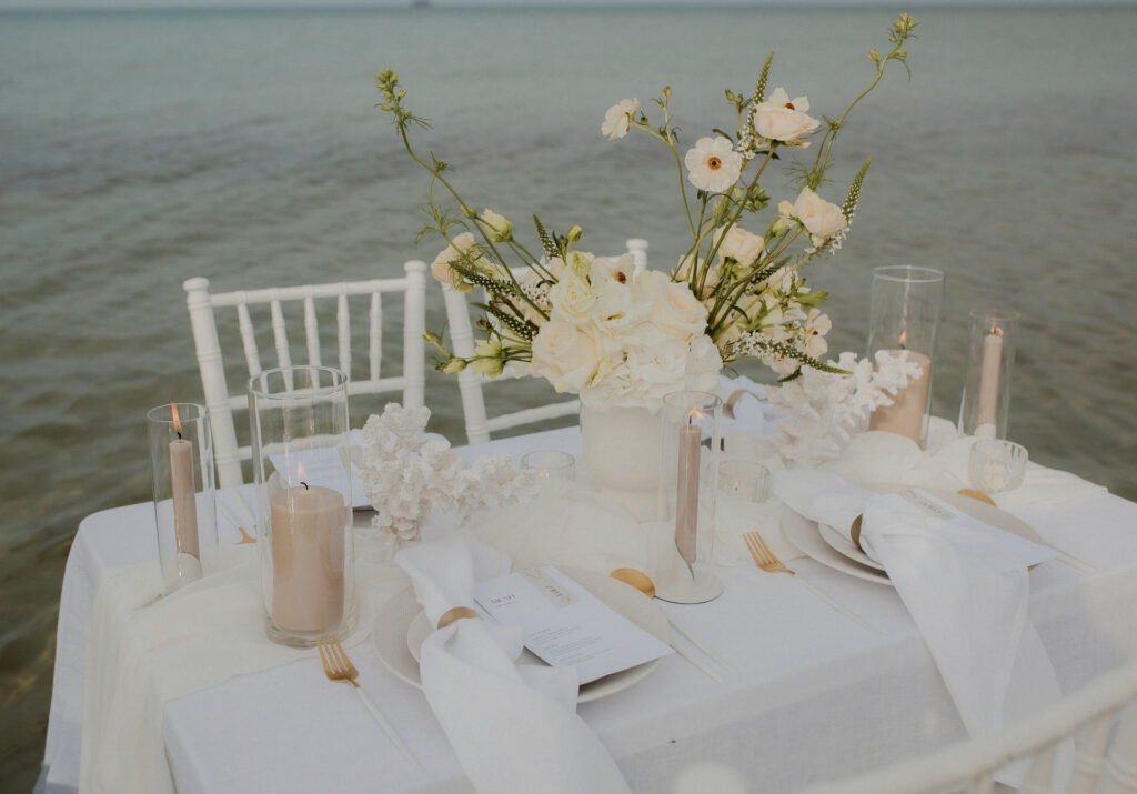 Eingedeckte Hochzeitstafel am Strand mit weißen Stühlen